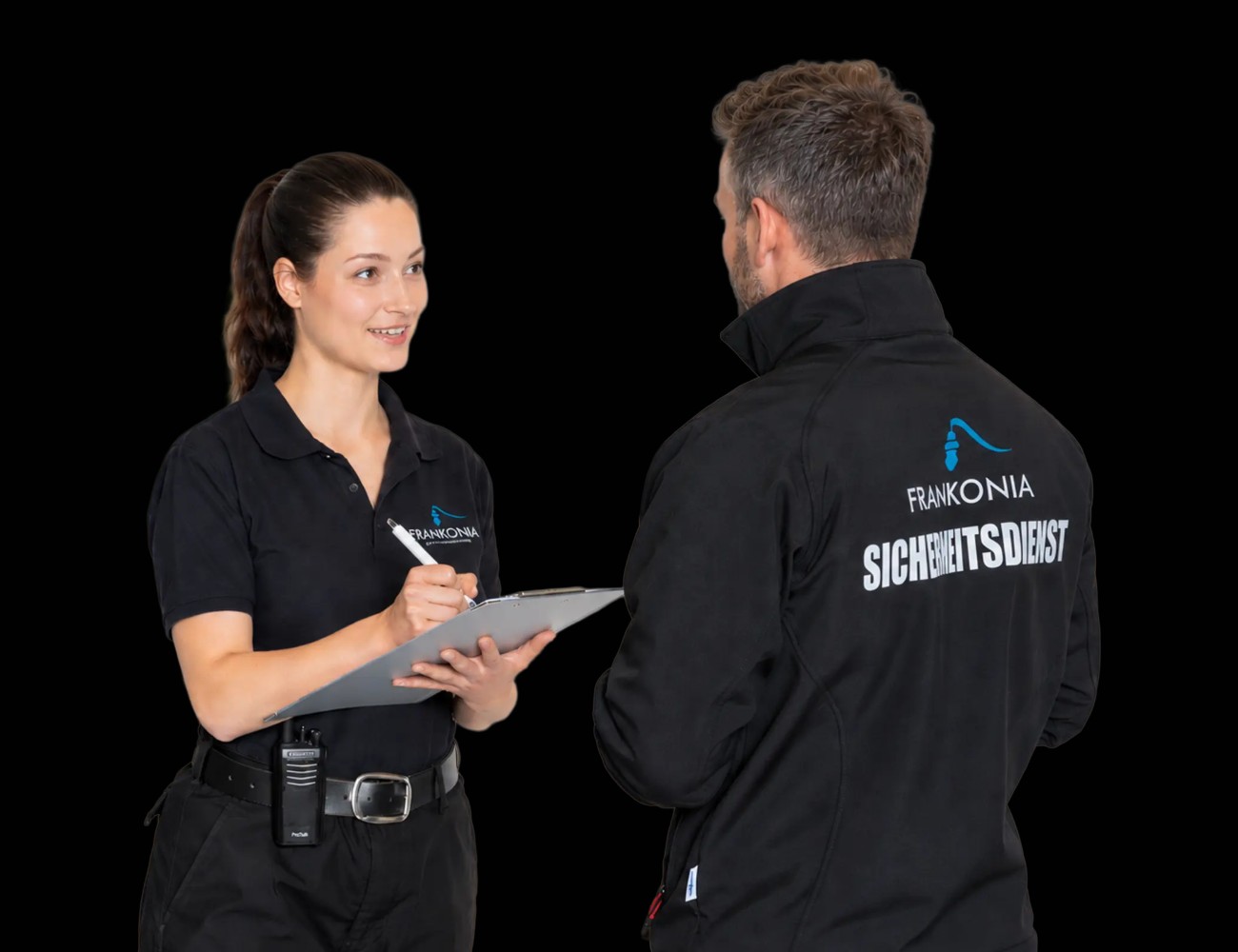 FRANKONIA Mitarbeiterin mit Klemmbrett im Gespräch mit einem Kollegen in Softshelljacke, vor schwarzem Hintergrund